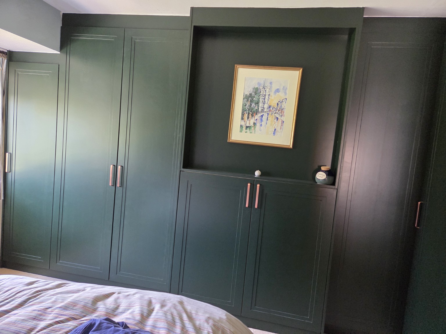 Bespoke dark green fitted bedroom wardrobes with integrated display alcove and copper-toned handles.