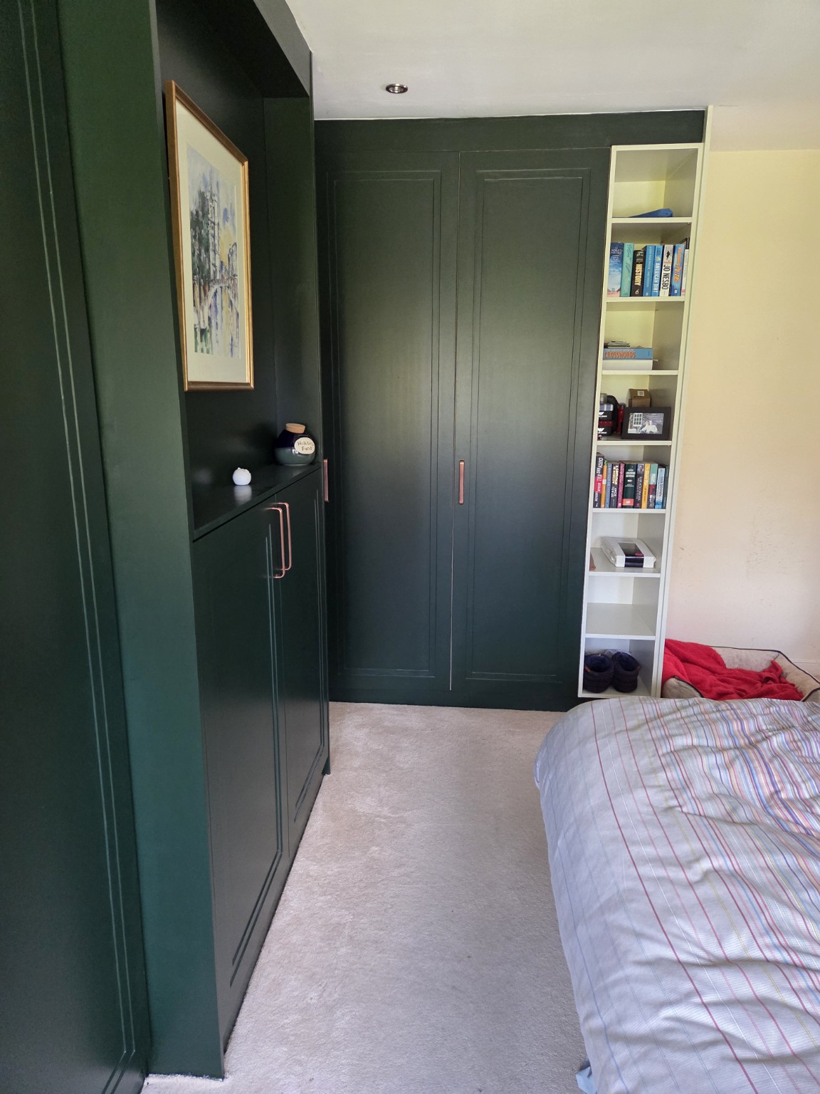 Side view of dark green fitted bedroom wardrobes with integrated shelving and storage.