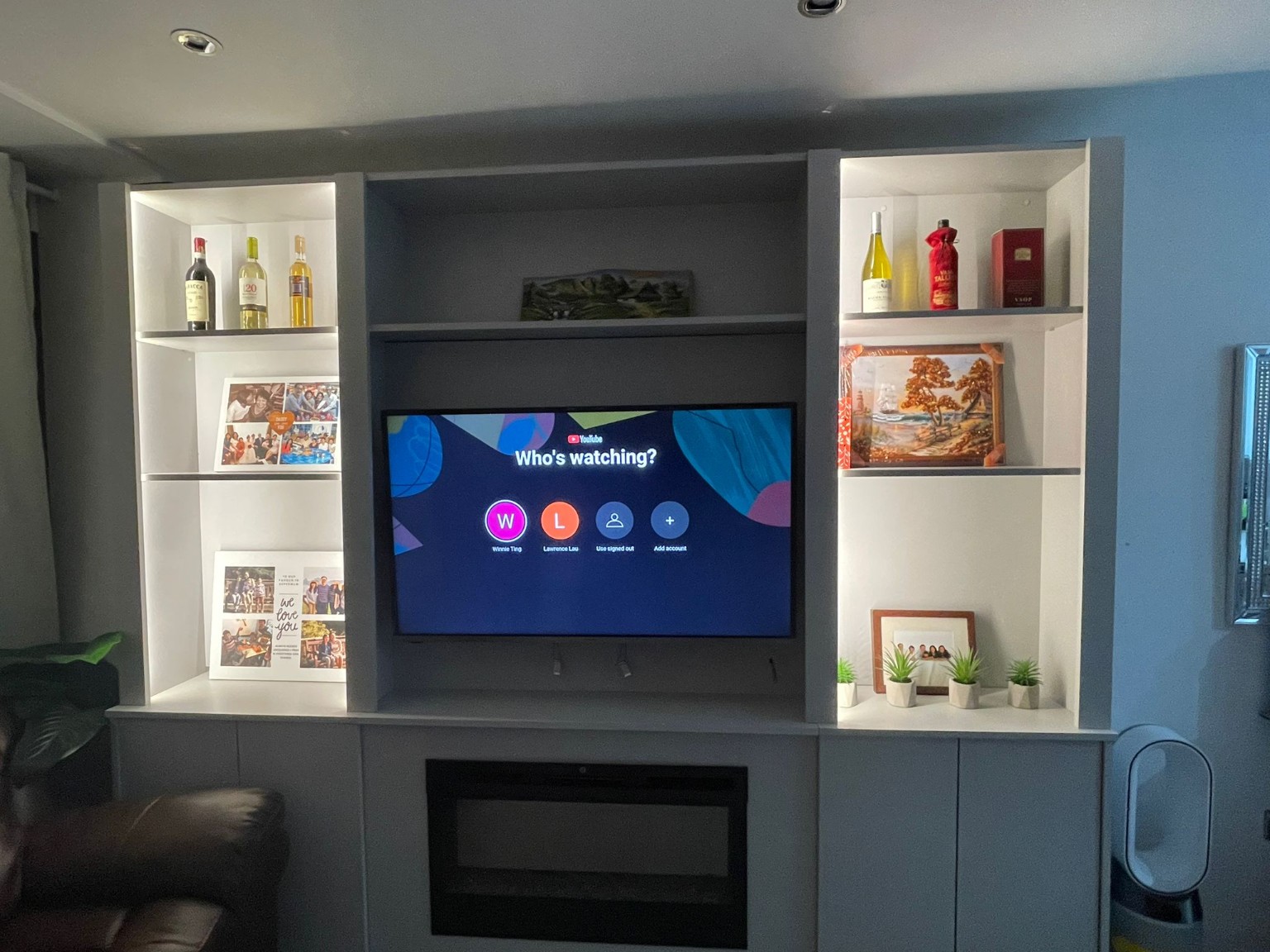 Bespoke grey media wall with illuminated display shelving, television and integrated fireplace.