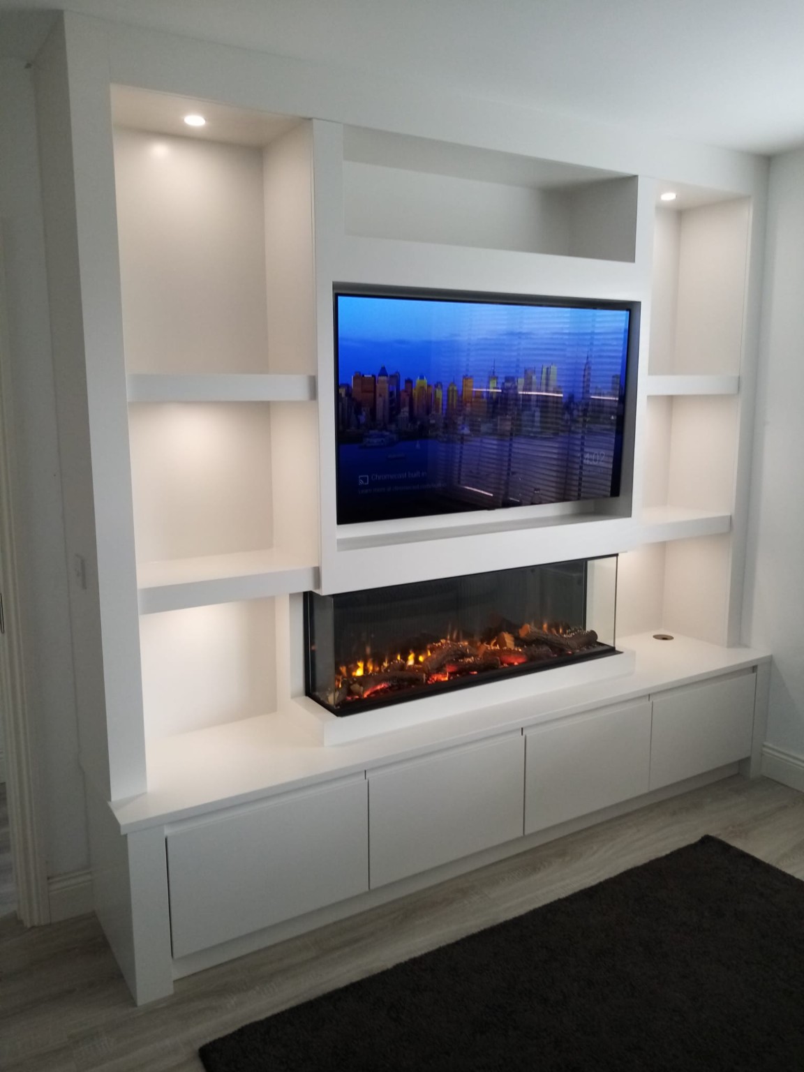 Bespoke white media wall with recessed television, electric fireplace, display lighting and concealed storage.